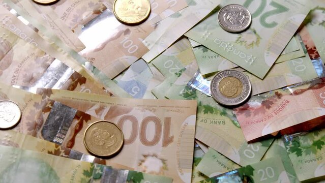 Canadian dollars and coins lie on banknotes of Canada of different denominations and rotate in a circle. Canadian banknotes of different values. Banknotes of Canadian currency. Dollar. Canada Money. 