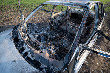 Obraz premium A burned out car. Burnt car in the field. Car fire, vehicle fire due to short circuit. Stolen car intentional arson. One vehicle was damaged in the fire.