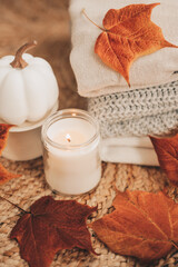 Obraz na płótnie Canvas Pile of folded warm autumn knit and cotton sweaters near a candle, pumpkin decor and colorful fall maple leaves