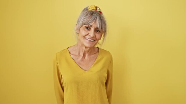 Confident middle age woman rocking grey hair in a pony tail, beaming with a cool, happy smile. a picture of joy and positivity against a vibrant yellow isolated background.