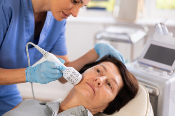 Mature female patient receiving professional hardware facial procedure at aesthetic medicine clinic...