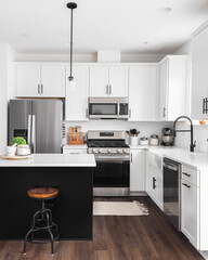 A modern farmhouse kitchen with white cabinets and a black island, stainless steel appliances,...