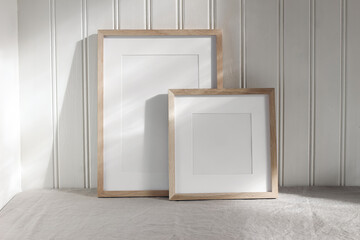 Set of blank vertical and square wooden picture frame mock ups in sunlight. White beadboard wainscot wall paneling background with shadows. Neutral Scandinavian home decor. Nordic interior.
