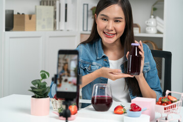 Smiling young beautiful Asian reviewing tasty mixed strawberry and cherry juice detox drinks,...
