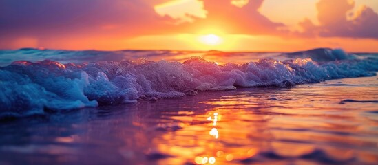 The sun is seen setting over the ocean waves, casting a warm golden glow on the water. The vivid waves reflect the colorful sky as the day comes to a peaceful end. - obrazy, fototapety, plakaty