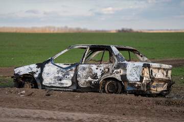 Fototapeta premium A burned out car. Burnt car in the field. Car fire, vehicle fire due to short circuit. Stolen car intentional arson. One vehicle was damaged in the fire.
