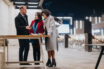 Obraz premium Three business people engage in a serious discussion at a contemporary outdoor location, sharing ideas and strategies at twilight.