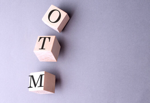 Word OTM -OUT OF MONEY on wooden block on the grey background