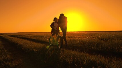 Mother teaches her child to keep balance while sitting on bicycle. Active Mom teaches her little...