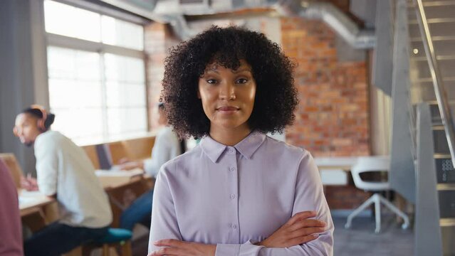 Portrait of businesswoman with serious expression working in modern open plan office looking at camera with colleagues in background - shot in slow motion
