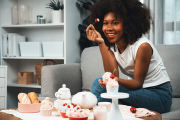 Obraz na płótnie Canvas Beautiful young African blogger presenting piece of cupcake in concept showing special cuisine in pastel color. Content creating of social media with favorite sweets bakery dish. Tastemaker.