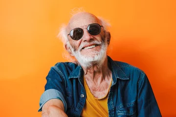 Fotobehang Front view of a happy senior man posing with optimism and sunglasses over colorful orange background © LorenaPh