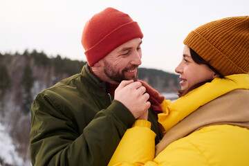 Medium closeup of happy bearded Caucasian man holding hands of his wife while standing outdoors on cold winter day