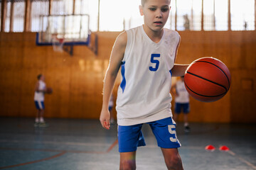 Portrait of an active junior athlete dribbling a basketball on court.