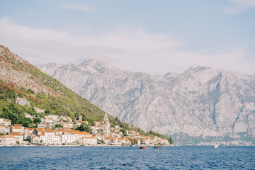 Ancient houses of Perast on the shore of the Bay of Kotor with an ancient bell tower against the backdrop of the mountains. Montenegro