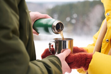 Unrecognizable male tourist pouring hot tea into mug for his wife on cold winter day, medium...