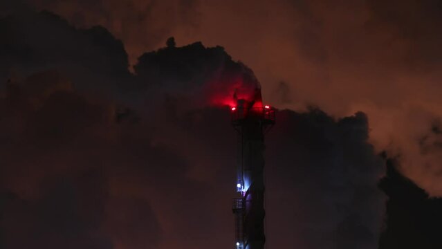 Industrial furnace chimney in a steam of cooling towers. Red aviation obstruction lighting. Night scene at extremely low temperature.