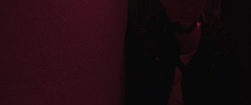 A wounded bald man with a gun breaths heavily in the red corridor