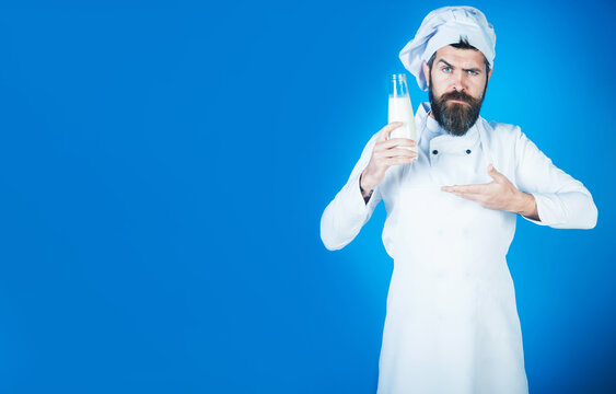 Chef man in uniform with bottle of milk. Dairy farmer products, chef recommendation, protein diet. Serious male cook in apron pointing with hand to bottle kefir or yogurt. Copy space for advertising.