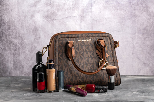 Women's Michael Kors brown handbag and accessories by the gray wall.