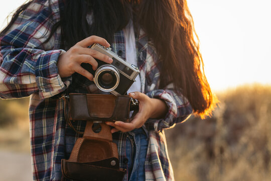 Unrecognizable woman taking photos with analog camera at sunset