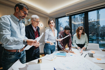 A team of multigenerational business colleagues collaboratively working over documents in a bright office space, displaying teamwork.