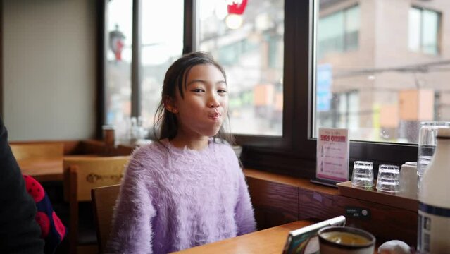 Hungry Korean teenage girl operating her smartphone and waiting while waiting for food at a restaurant in Seoul, South Korea 大韓民国ソウルのレストランで料理を待つ間にスマートフォンを操作して待つ空腹の韓国人の１０代の少女