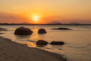 Sunset over a tropical beach with rock silhouettes, reflections, and an orange glow at Grey's Beach...