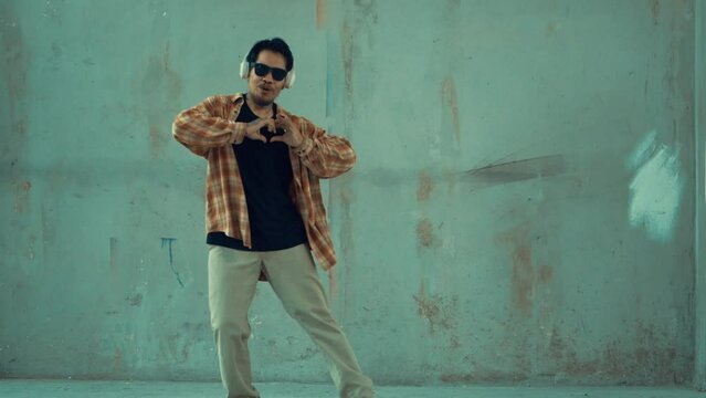 Attractive hispanic dancer in casual look practice street dance while listen music from headphone at cement background. Motion shot of break dancing performance. Outdoor sport 2024. hiphop.