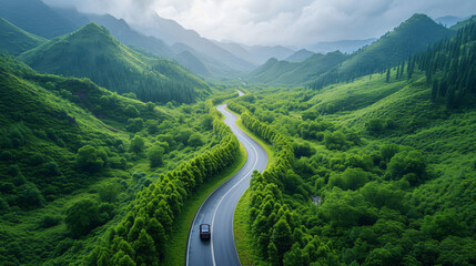 EV (Electric Vehicle) electric car is driving on a winding road that runs through a verdant forest and mountains - obrazy, fototapety, plakaty