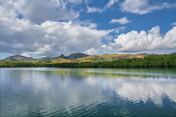 Achang, Guam, a village on the south tip, shot  from the ocean with calm seas and fluffy clouds and a view of the mountain range.