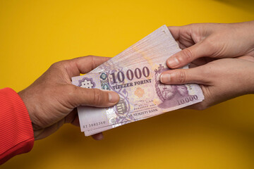 A man holds a stack of Hungarian paper forints in his hand. Against a yellow background. Concept...