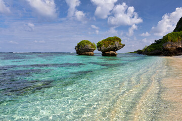 Clear warm waters and mushroom rocks at Tanguisson Beach, Guam on a clear sunny day with fluffy clouds