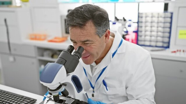 Mature male scientist analyzing samples through a microscope in a modern laboratory.