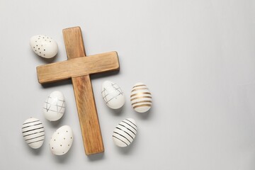 Wooden cross and painted Easter eggs on light grey background, flat lay. Space for text
