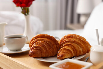 Tasty breakfast served in bed. Fresh croissants, coffee and honey on wooden tray, closeup