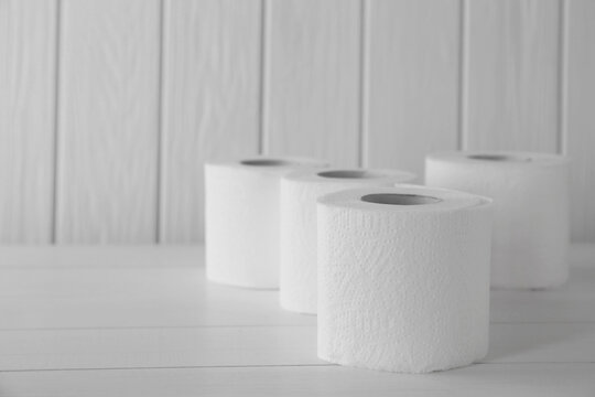 Many soft toilet paper rolls on white wooden table. Space for text