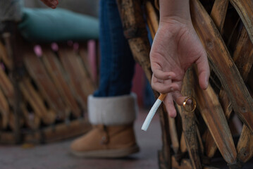 Mujer con cigarrilo en mano, sosteniendo anillo de matrimonio, contemplando el divorcio. - obrazy, fototapety, plakaty