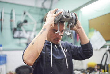 Portrait of an hispanic young worker removing a respiratory protection mask, as he finishes a spray painting job in his workshop. Health protection in industrial work. Real people working.