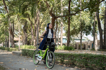 Fototapeta na wymiar A young Asian woman commutes to work by cycling in a green city, carrying a backpack and using a reusable drinking cup to avoid harming the environment.