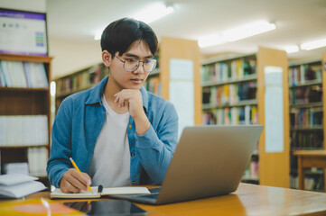 Male college students are working on laptops and searching for books to study, make reports, find useful information in college room. Concept of reading, learning and intelligence.