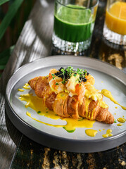Delicious croissant with egg benedict or poached egg, black caviar, shrimps and microgreens on plate on marble table with smoothies. Healthy breakfast food, diet, top view