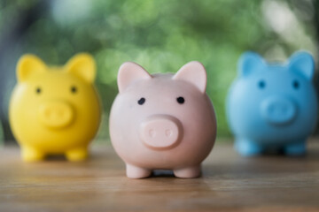 Pink piggy bank in front of yellow and blue piggy bank. Decision making for saving concept. Money boxes on a table
