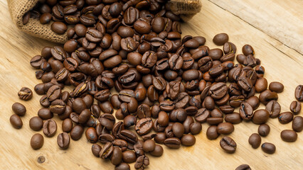 Obraz premium Roasted Coffee Beans Spilling Out of Burlap Sack onto Wooden Table