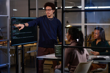 Group of three young ethnically diverse IT specialists working together on code in office late in evening