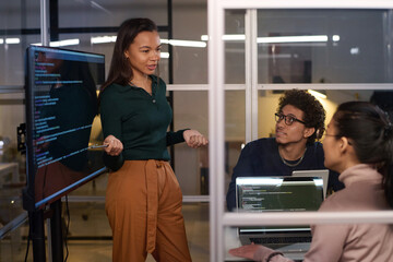 Ethnically diverse programmers working together on code at workplace in IT company office late in evening