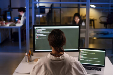 High angle rear view of unrecognizable young female programmer working on code using desktop...