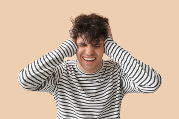 Young man suffering from headache on beige background