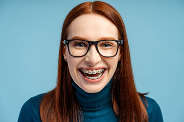 Redhead woman with braces, donning glasses, laughing while looking at the camera