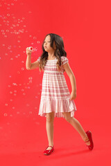 Cute little girl blowing soap bubbles on red background